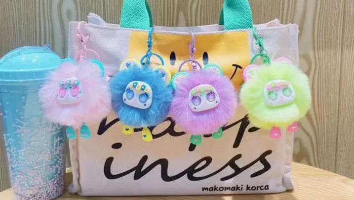 Bag with colorful pom-pom keychains and a blue tumbler on a wooden surface